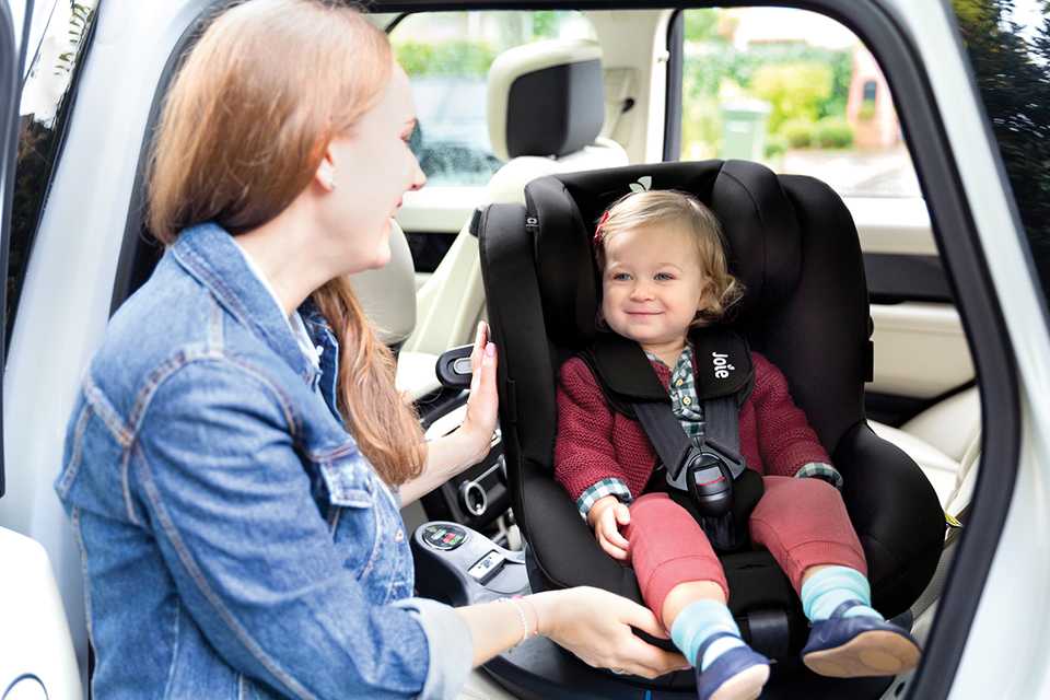 A mother looking at her child who is strapped into a car seat.