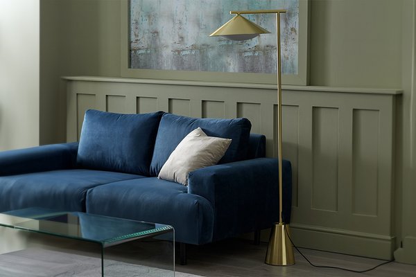 Gold floor lamp in living room next to blue velvet sofa.