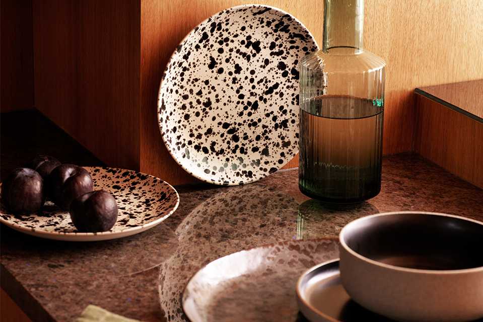Speckled white and black tableware stacked on marble kitchen counter in a cosy and warm kitchen setting.