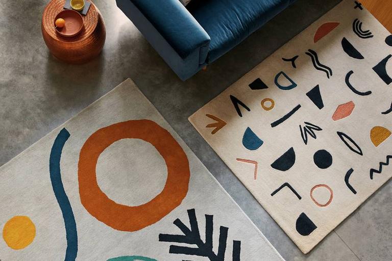 Image of 2 rugs with abstract design next to blue sofa.