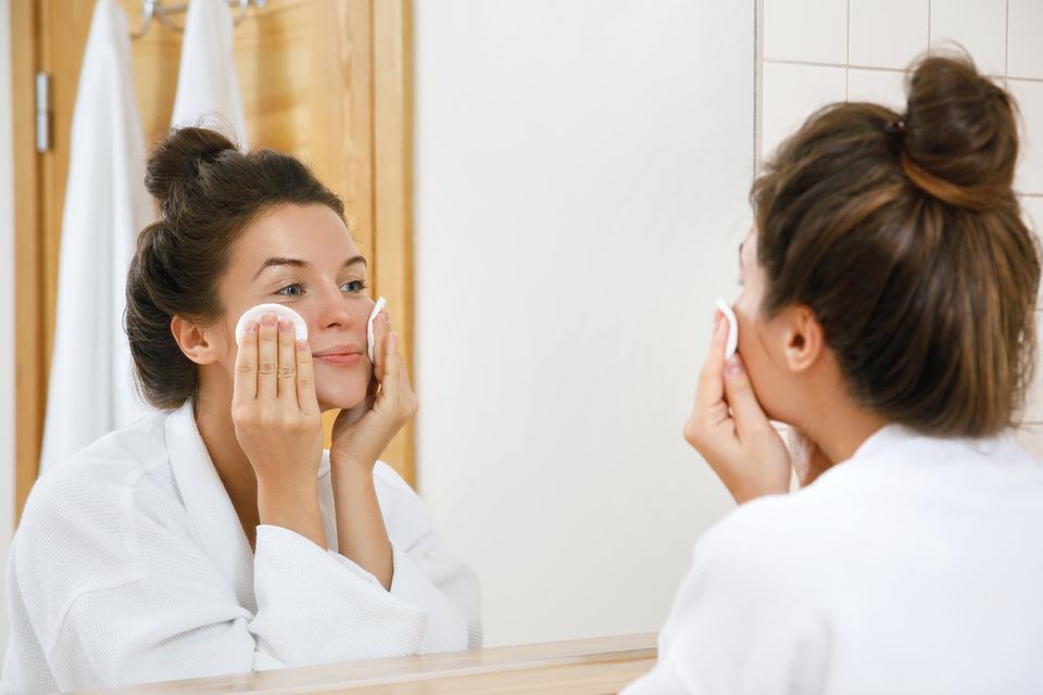 Woman looking in mirror and removing makeup.