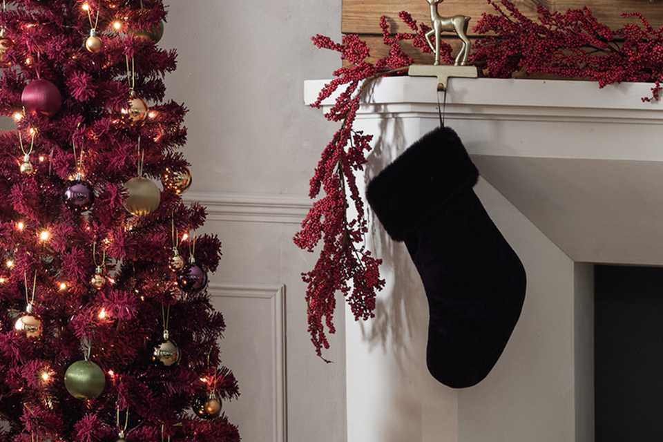 A Habitat burgundy Christmas tree next to a stocking hung by the fireplace.