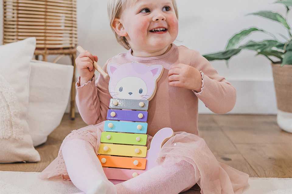 Little girl playing with Our Little World wooden sensory cat xylophone.