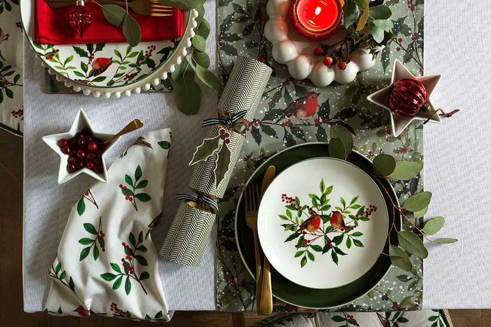 A table set with Habitat Red Robin red and green plates, bowls, and candles.