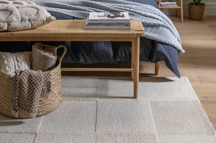Habitat Checkerboard rug in neutral tones, placed in a bright, modern living room. The wool rug features a bold high-low checkerboard pattern with a soft cut pile texture, adding warmth and visual interest to the wooden floor.