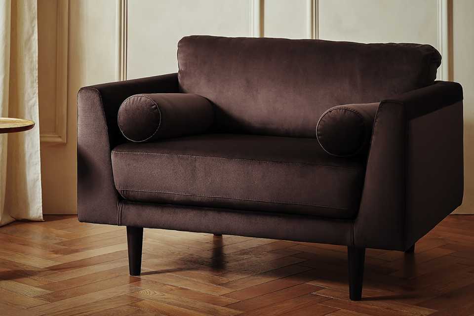 Modern brown armchair with bolster cushions, set on wooden flooring in a light-toned room.