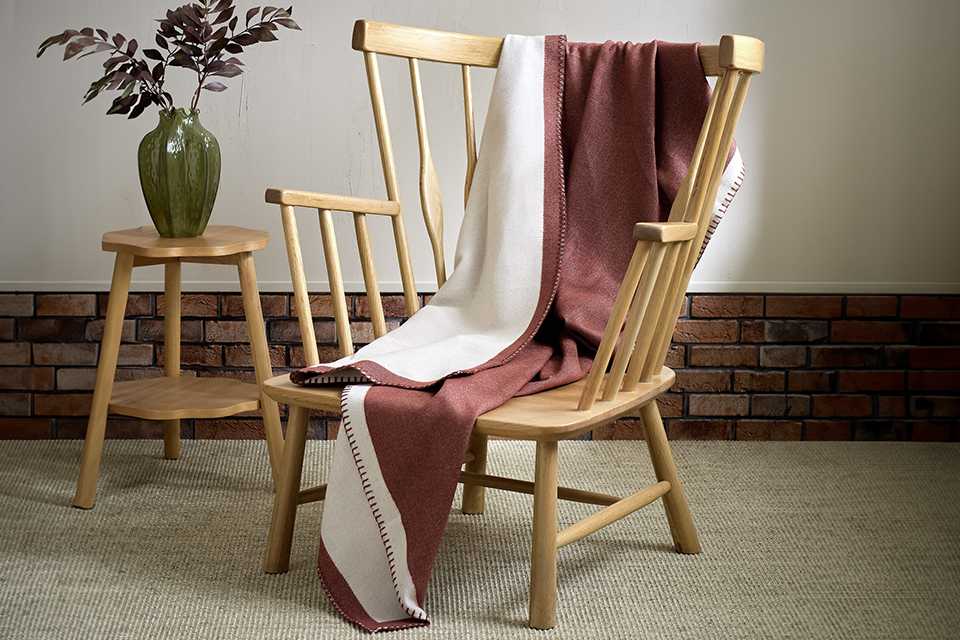 Blush pink throw draped over a wooden armchair, showcasing its soft texture and cosy appearance in a modern living room setting.