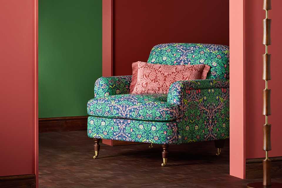 Green floral print armchair with red floral cushion on and wooden wheel legs.