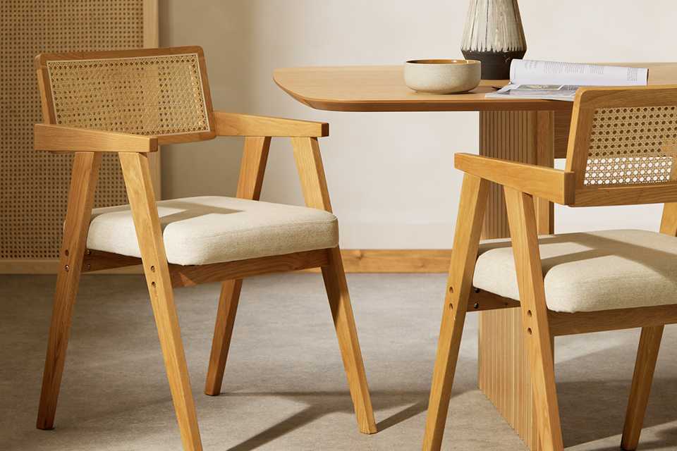 Rattan wicker dining chairs wih white cushioned seat.