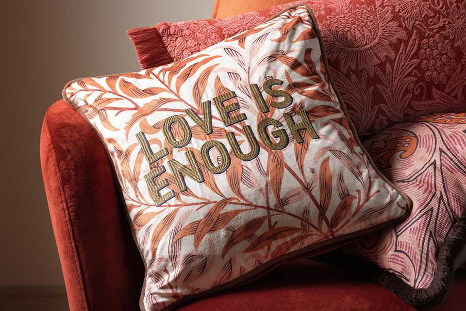 Love is enough text cushion on orange floral background.