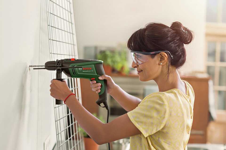 A woman using Bosch Corded Universal Impact Hammer Drill on a wall.