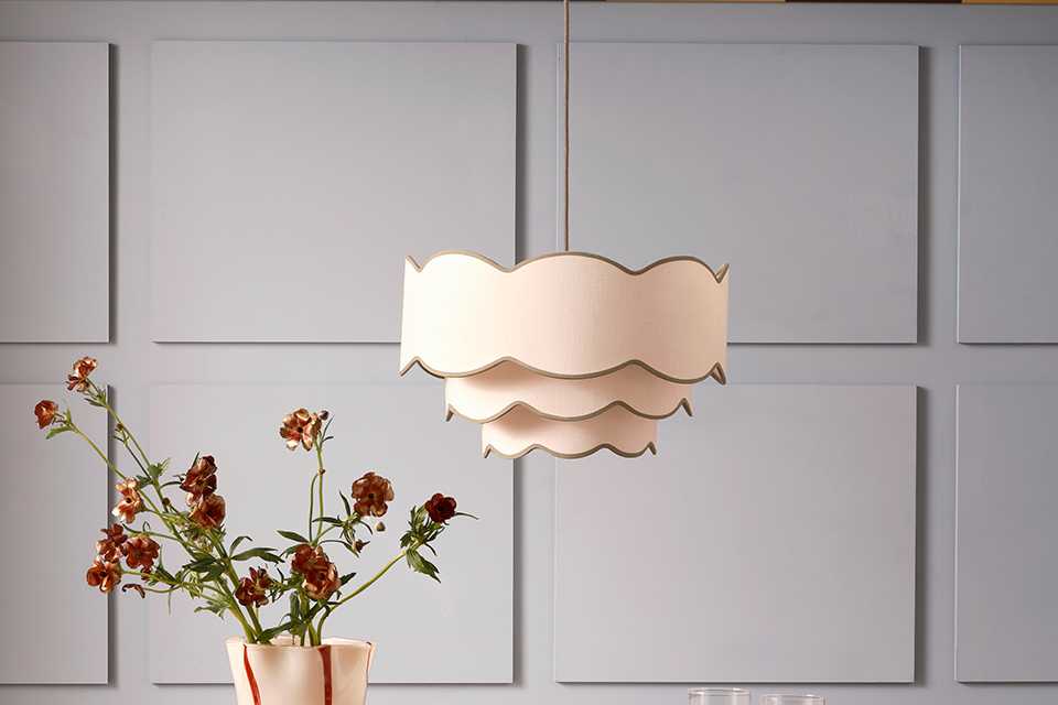 A Habitat ceiling light in a dining room above a table with plates, glasses and flowers in a vase on top of it.