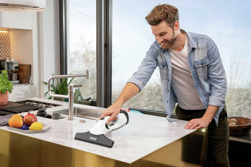 A man using a Karcher handheld window vacuum cleaner to clean a worktop in his kitchen.
