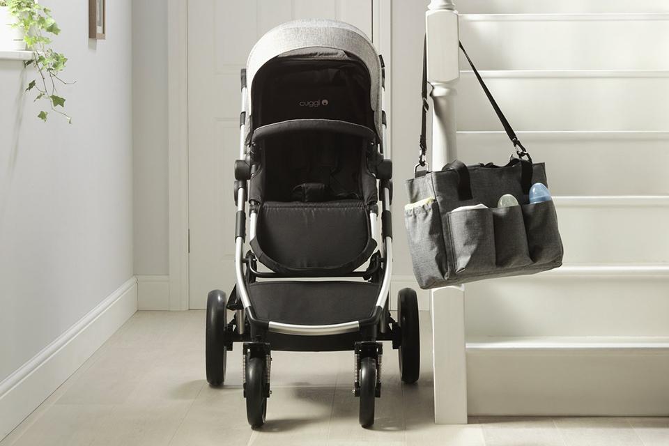 Grey and black pushchair in hallway with baby bag hung on banister.
