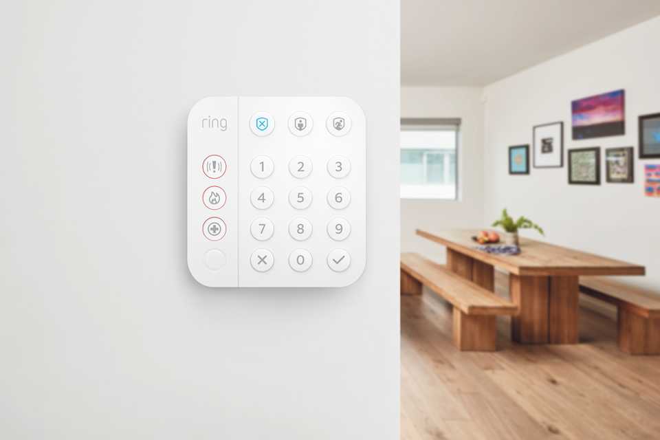 Ring Alarm keypad installed on a whilte wall in a living room setup.