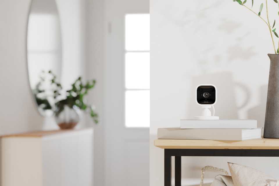 A while Blink Mini indoor camera placed on a wooden table with other things in a room.