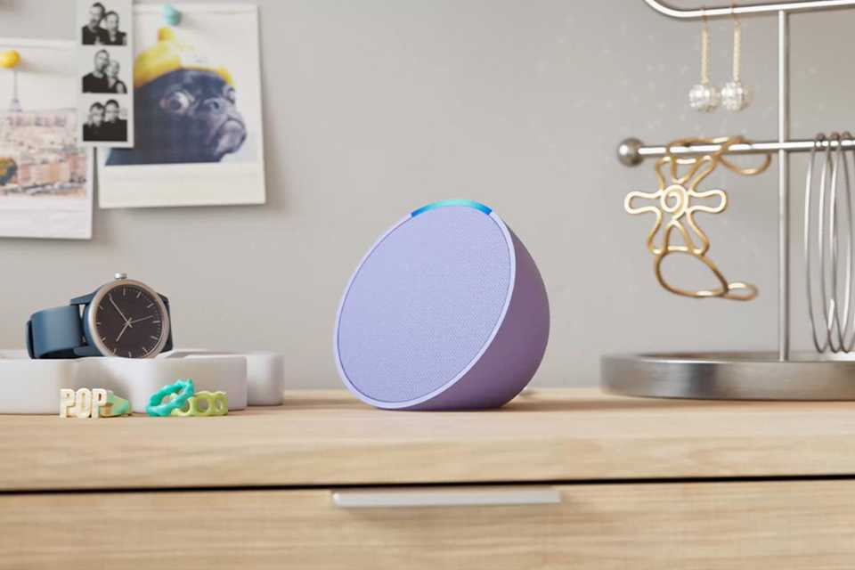 A purple Amazon Echo Pop smart speaker with Alexa placed on a dressing table with other things.