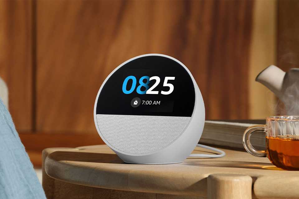 A white Amazon Echo Spot smart alarm clock with Alexa placed on a wooden bedside table.