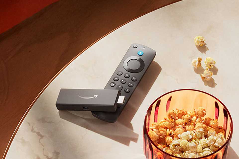 An Amazon Fire TV stick placed on a table beside a tub of popcorn.