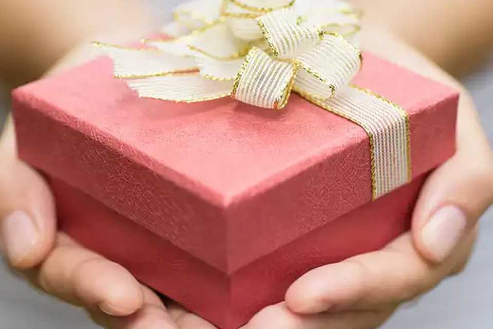 A person holding a gift box with a bow on top.