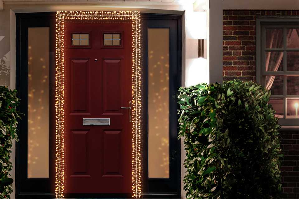 A silver wreath and warm white LED Christmas cluster lights on a door.