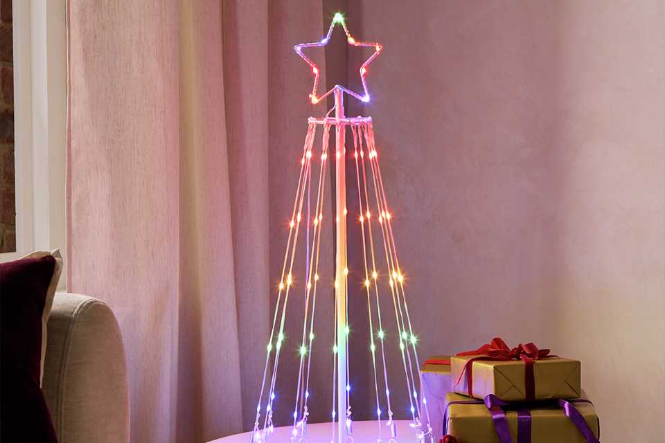 A Habitat Rainbow Light Up Christmas Tree Cone near gifts on a round coffee table.