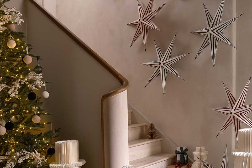Christmassy decor like paper stars, snowman and gift boxes near a Christmas tree and a stairway.
