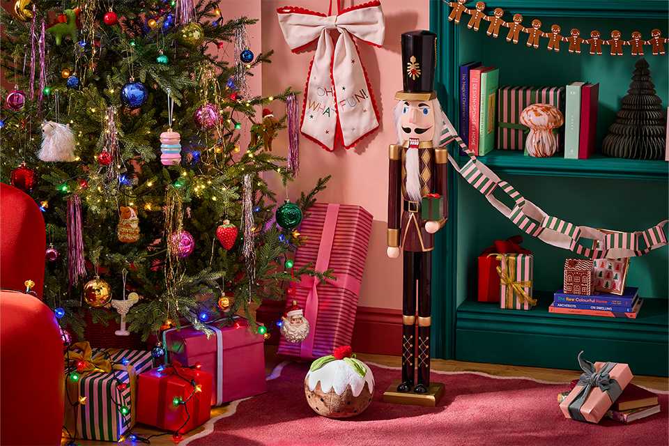 Colourfully decorated Christmas tree with wrapped gifts, a wooden nutcracker, Christmas pudding decoration and festive garlands.