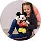 A girl holding a Mickey Mouse soft toy and smiling.