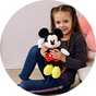 A girl holding a Mickey Mouse soft toy and smiling.