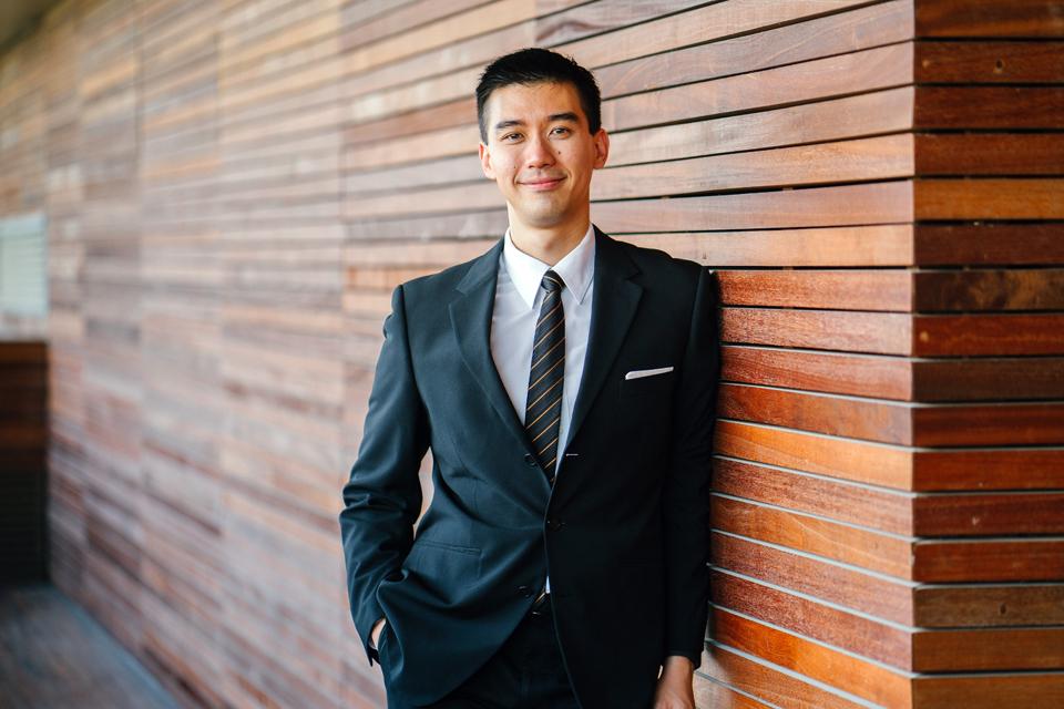 A man in a smart suit leaning against a wall.