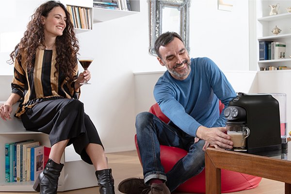 A couple enjoying a cup of coffee with a Lavazza coffee machine placed next to them.