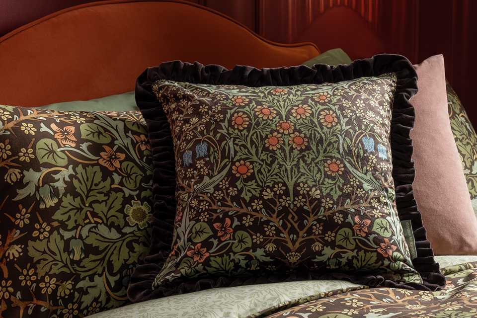 Morris and co cushion in floral pattern on bed in red bedroom.