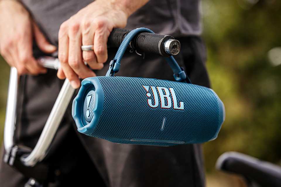 Blue JBL Charge 6 speaker hanging from bicycle handle bar driven by a man.