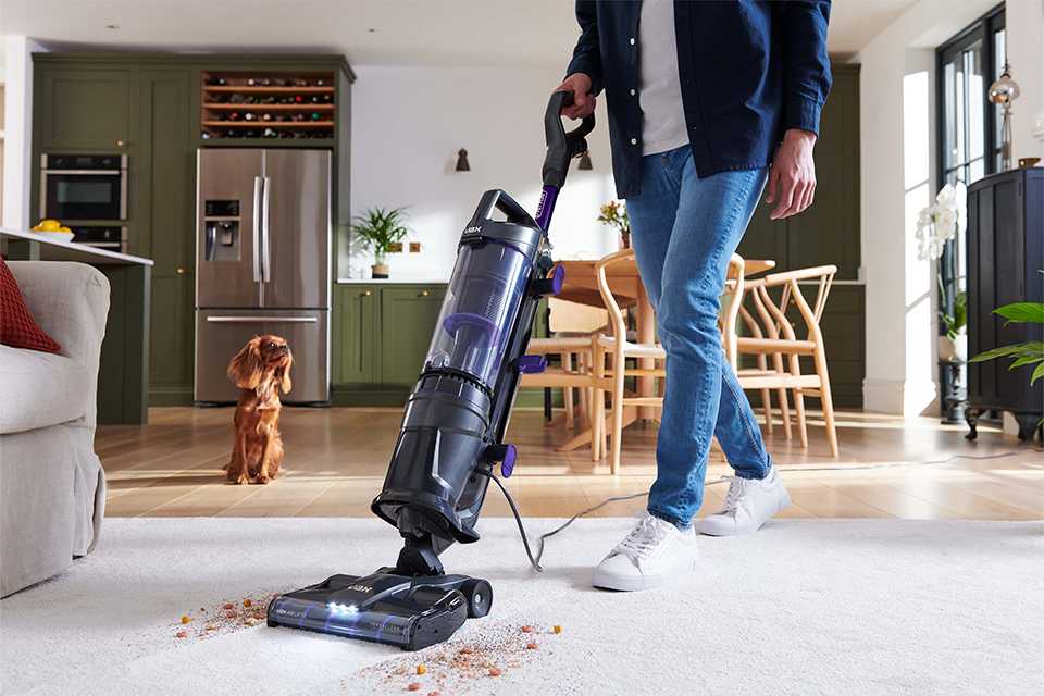 A shot of a person using Vax corded upright vacuum cleaner on a linoleum floor.