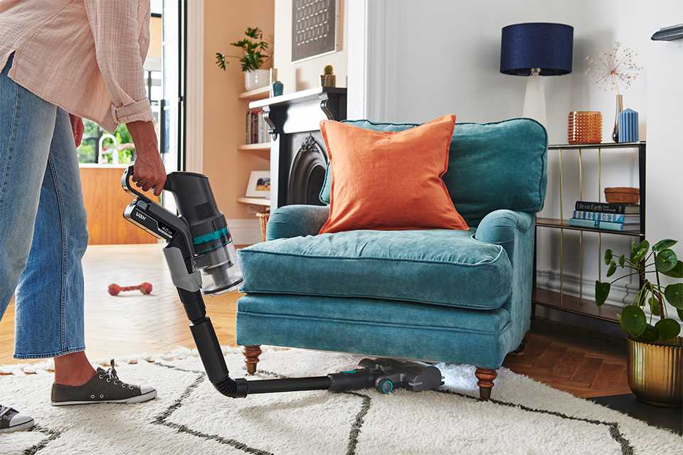 Someone using Vax vacuum cleaner under the sofa.