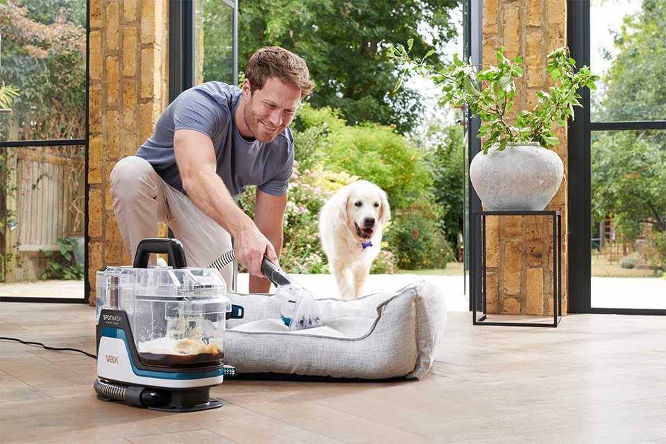 A man using Vax vacuum cleaner with a pet dog standing next to him.