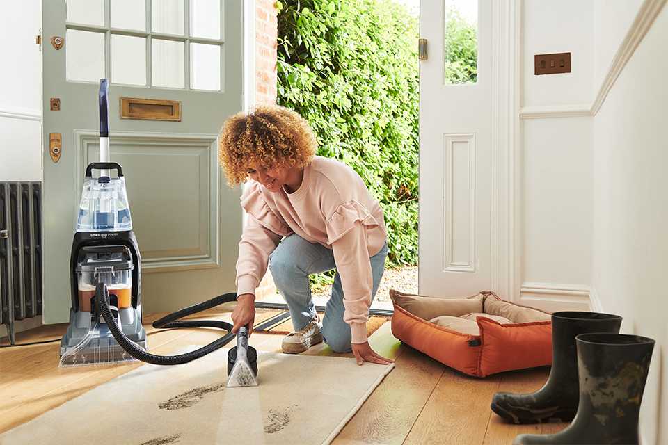 A woman using a corded vacuum cleaner on the carpet.