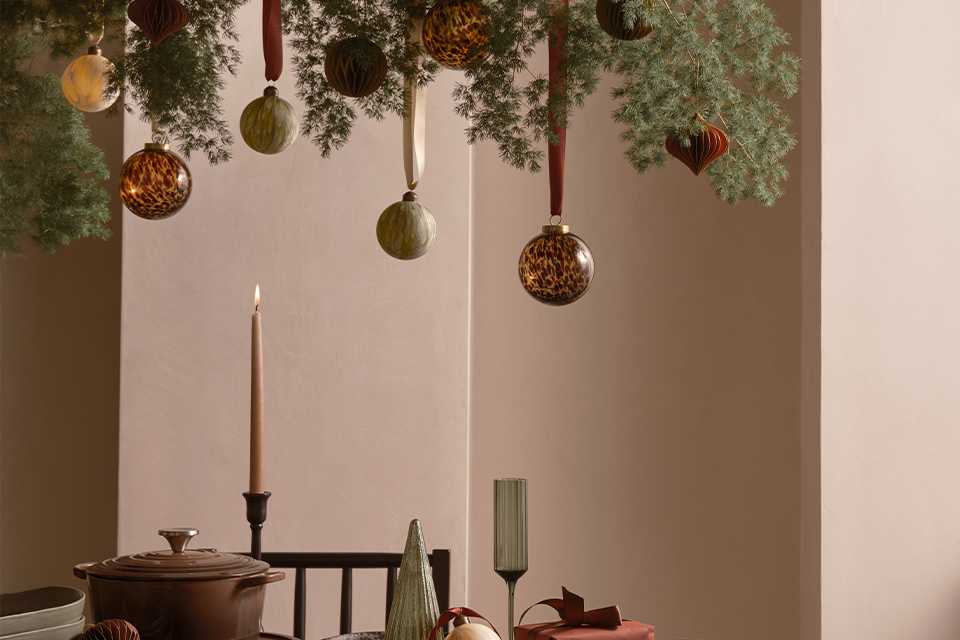 A table with glasses, plates and serveware and Christmas decorations hanging on top.