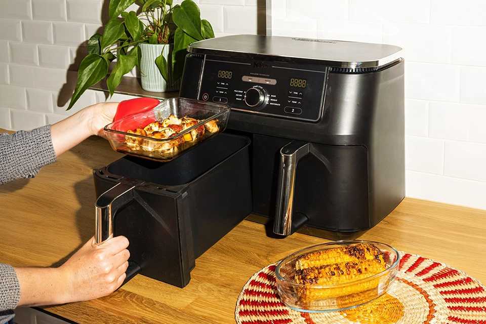 A person placing a Pyrex rectangular glass air fryer dish with chicken in it into an air fryer.