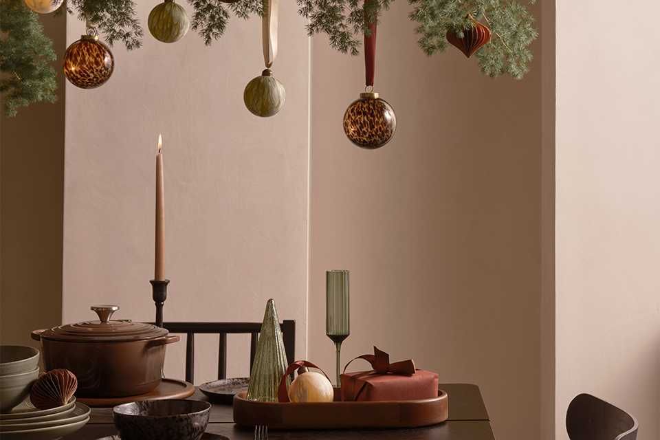 A table set up for hosting with baubles and Christmas decorations as well as stylish tableware and glasses.