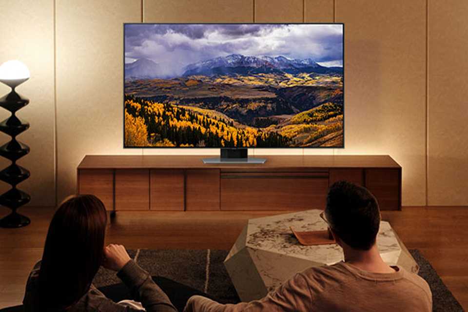 A Samsung QLED 4K smart TV on a TV wall mount in front of a young couple.