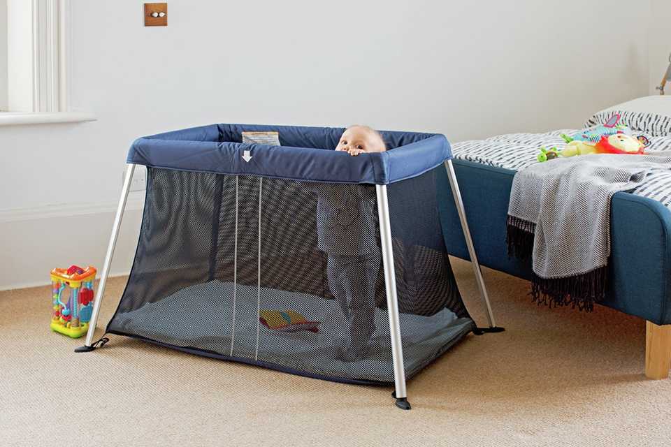 A baby in a Cuggl Deluxe Superlight Travel Cot.