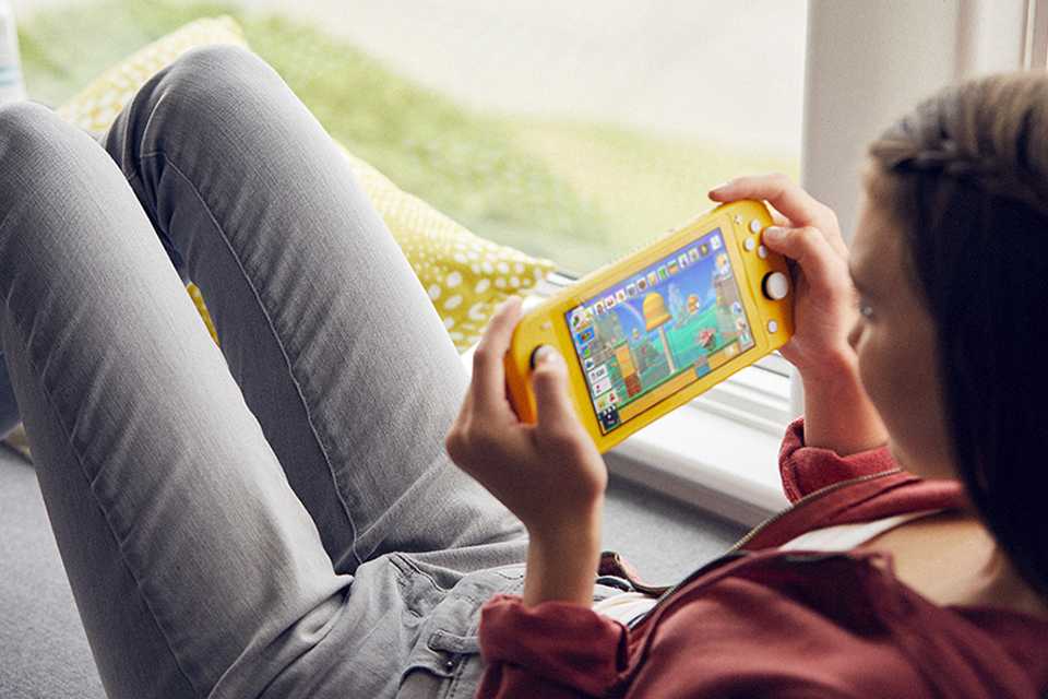 A girl playing on her yellow coloured Nintendo Switch Lite Handheld Console at a window.