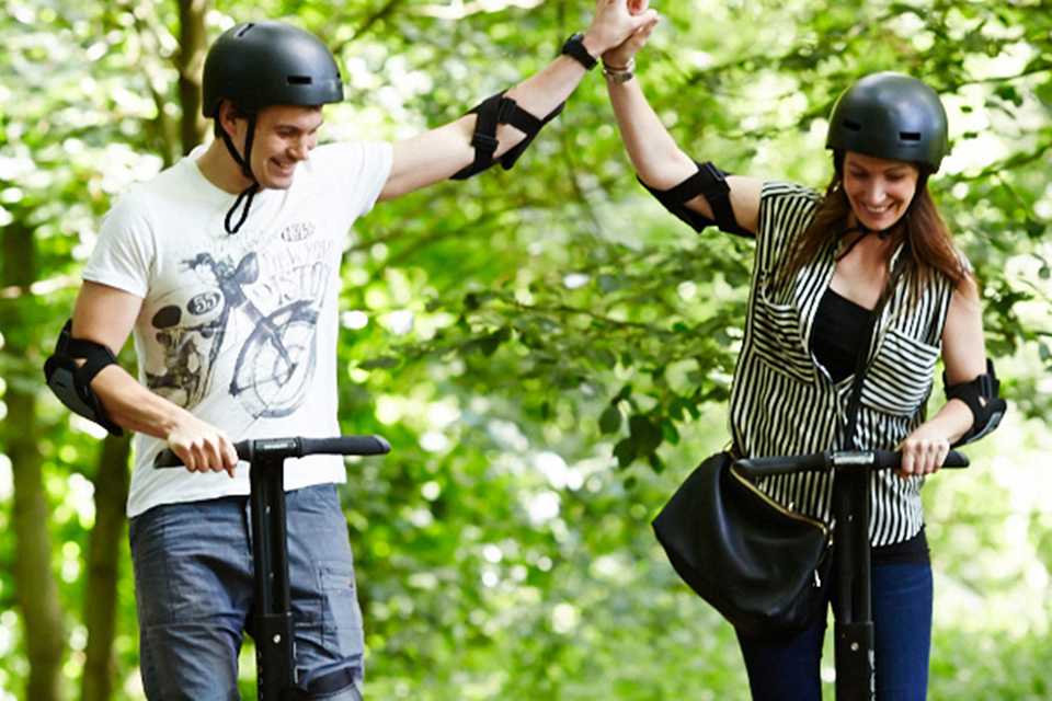 A happy couple in helmets enjoying a ride on segway in a park.