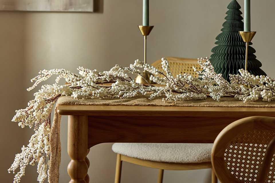 A table decorated with a Habitat white berry garland and some candlesticks.