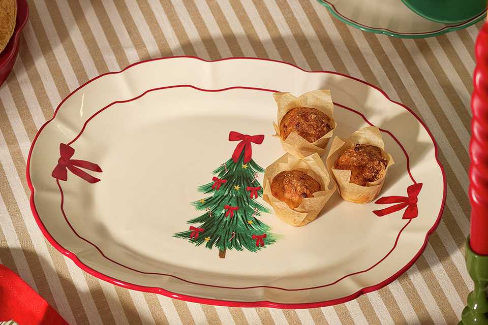 A serving plate with bows on the sides and a Christmas tree motif placed on a striped tablecloth.