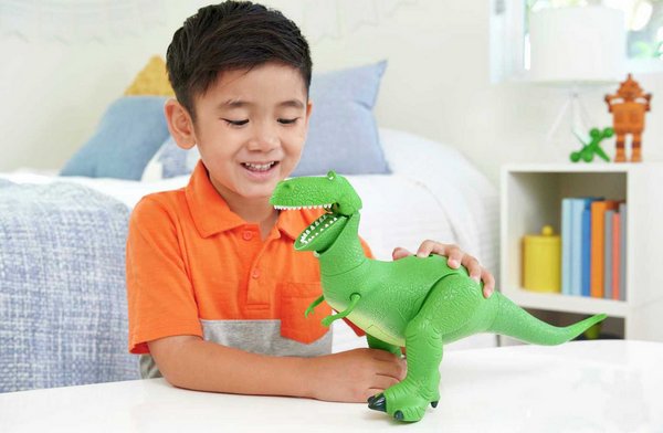 A boy in an orange shirt playing with a dinosaur toy in a bedroom.