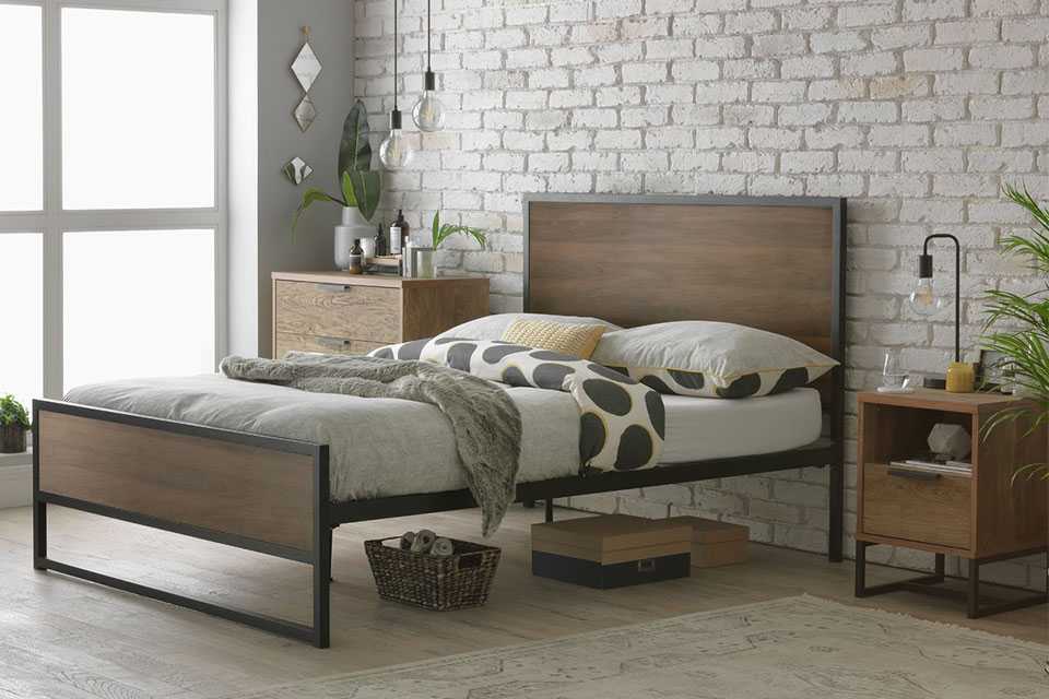 A metal framed, wooden bed with white and polka dot print bedding, pillows and a woolen throw on it.