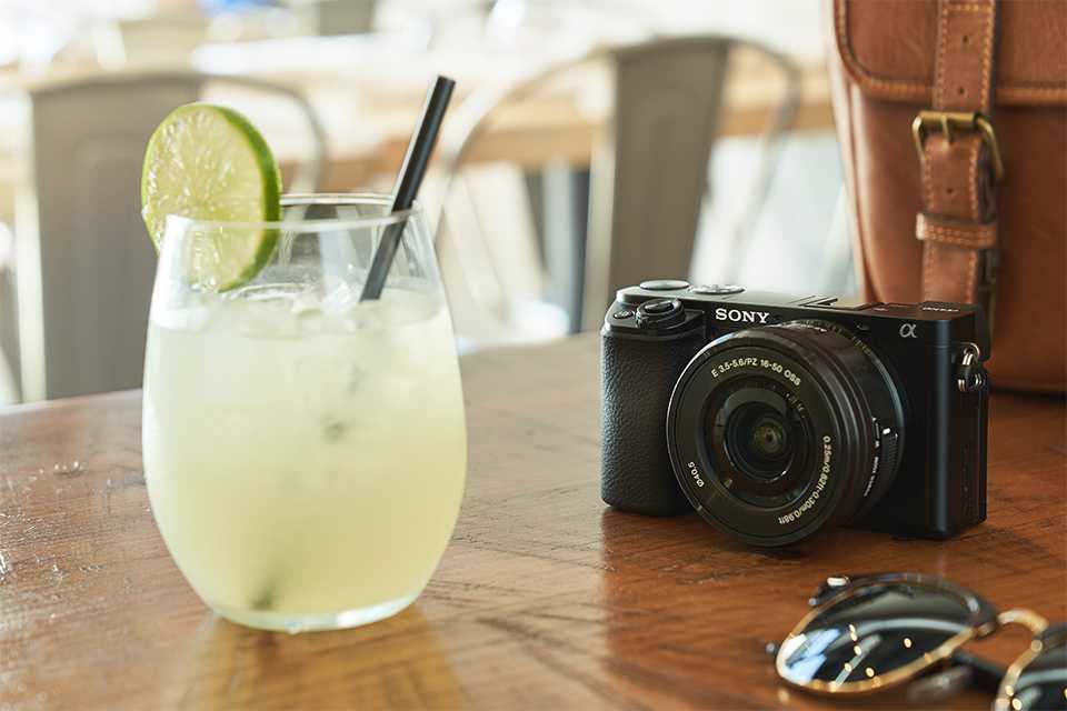 A Sony APS-C camera placed on a table next to a glass of lemonade.